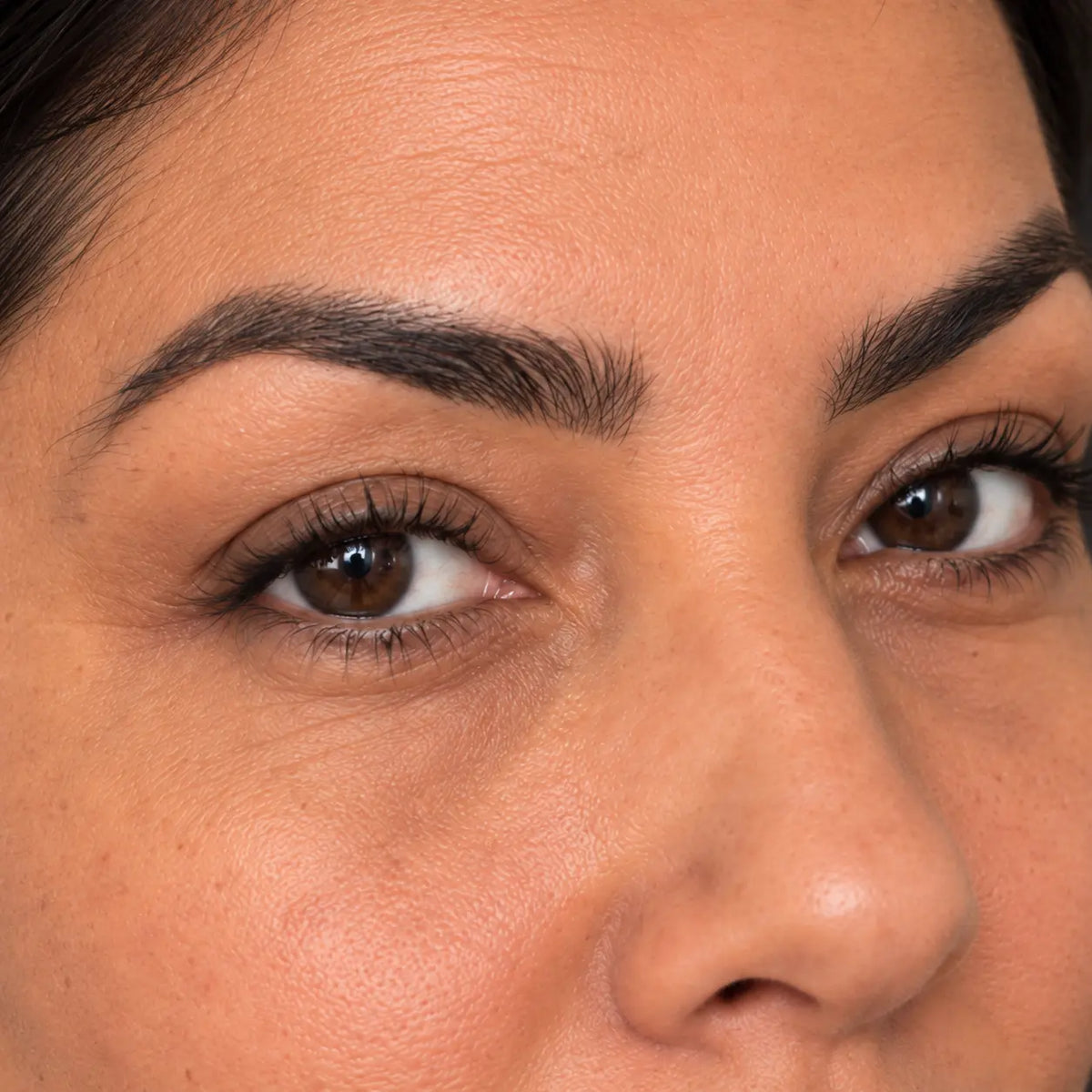Gros plan de trois-quarts sur les yeux bruns d’une femme et les nuances de sa peau sous les yeux.