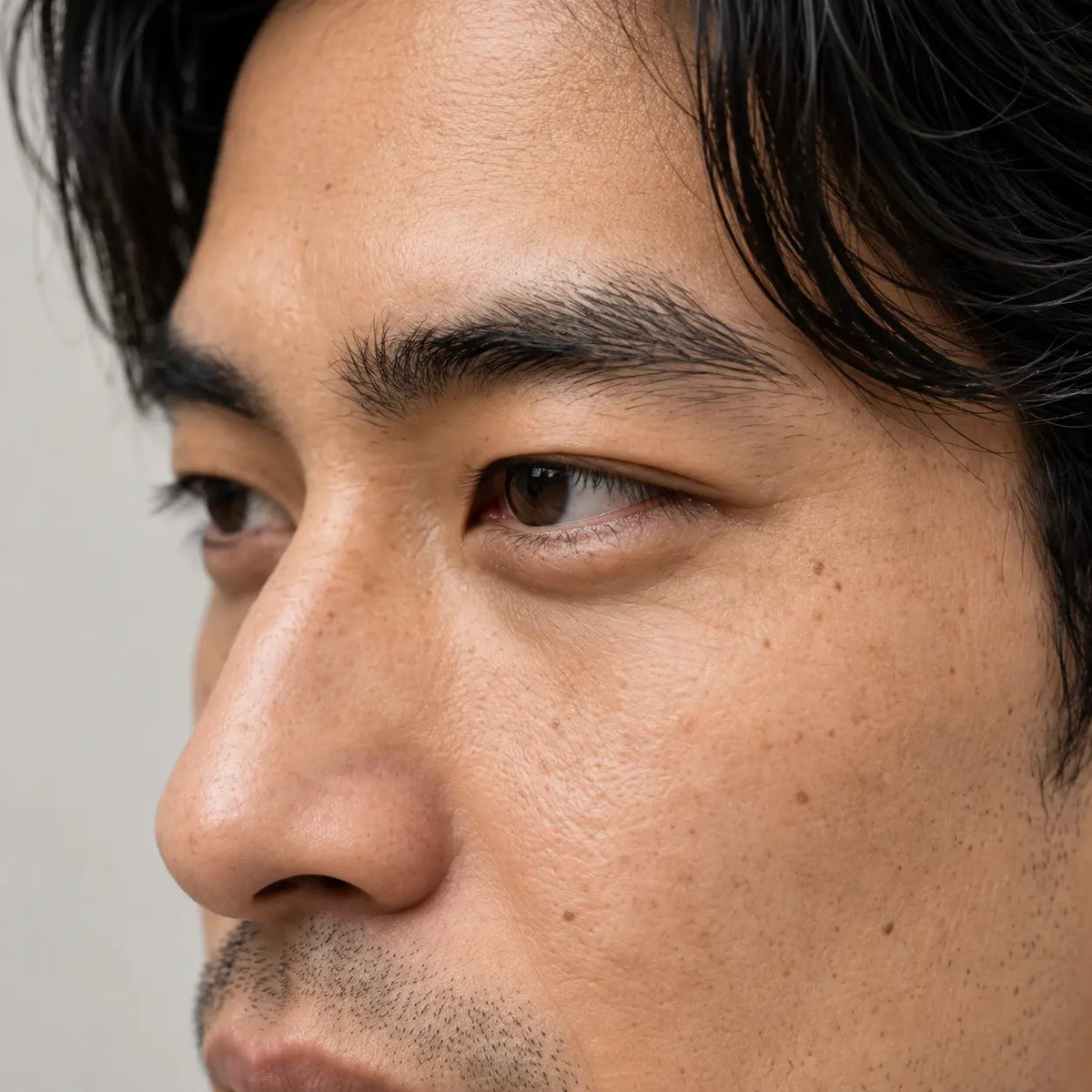 Gros plan de trois-quarts sur un homme aux cheveux noirs, le regard légèrement baissé et le contour des yeux visible.