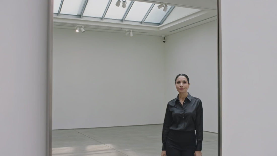 Femme élégante traversant une galerie d'art épurée, allure sobre et confiante, univers premium du Sérum Contour des Yeux Alternative Rétinol Glimoir