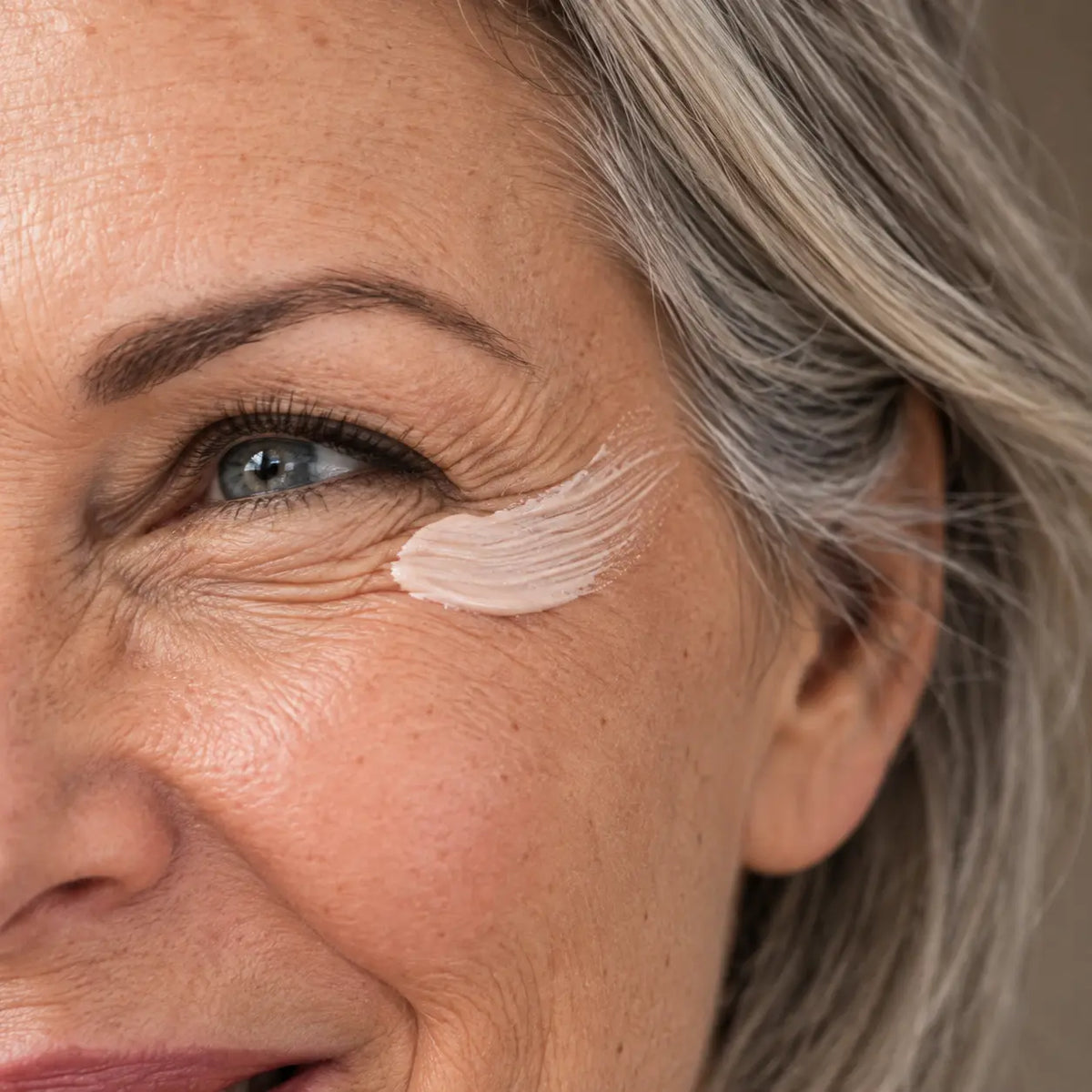 Routine anti-âge Glimoir : trait de crème fermeté sur les pattes d'oie d'une femme qui rit